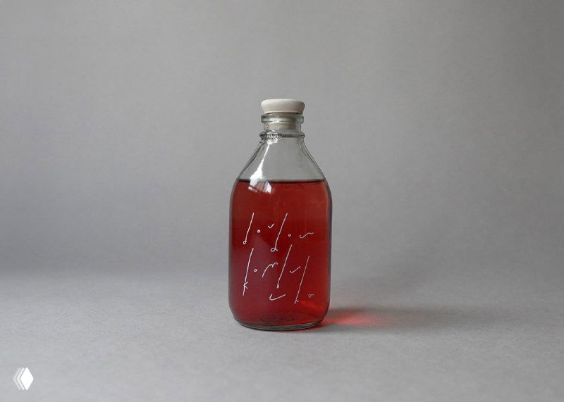 Простая стеклянная бутылка с красным напитком на сером фоне: лаконичная подача продукта в контексте визуальной системы бренда Dou dou.