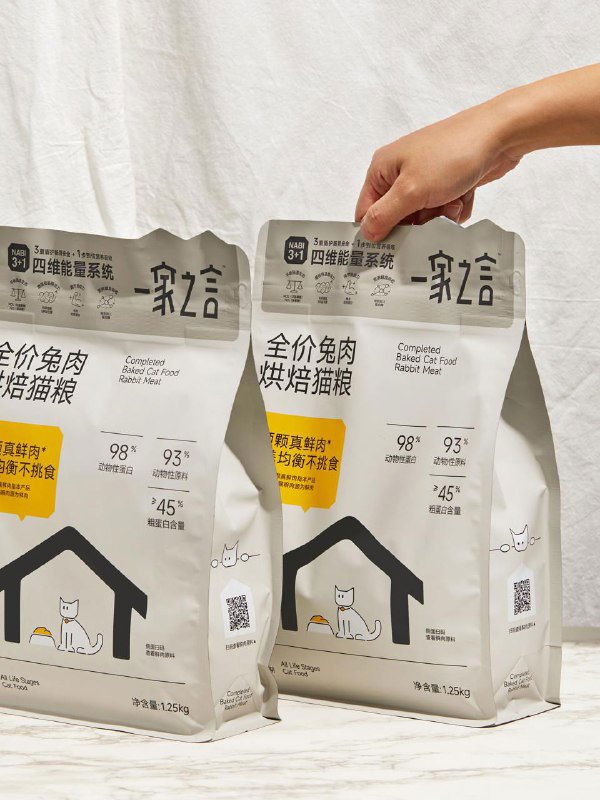 Две упаковки Home Cat Food в руках и на столе; изображение демонстрирует масштаб продукта и взаимодействие с пользователем при открытии