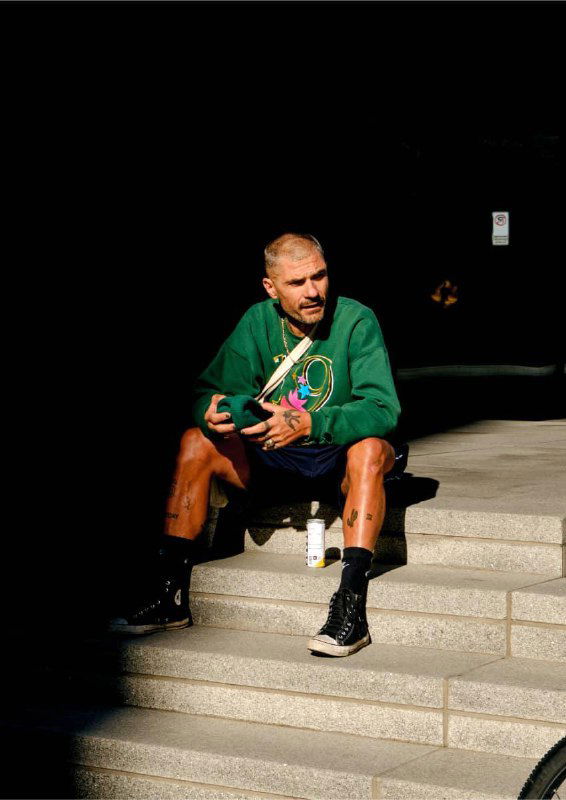 Уличная съёмка: мужчина в повседневной одежде сидит на ступенях рядом с элементами кампании Escape, контрастный свет и городской фон.