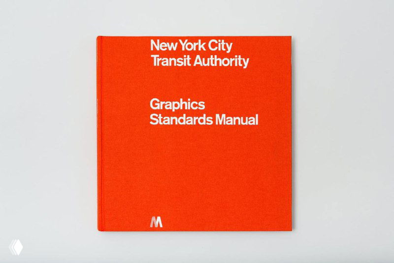 Фотография квадратной красной обложки книги с белым титулом "New York City Transit Authority Graphics Standards Manual" на ней, вид сверху.