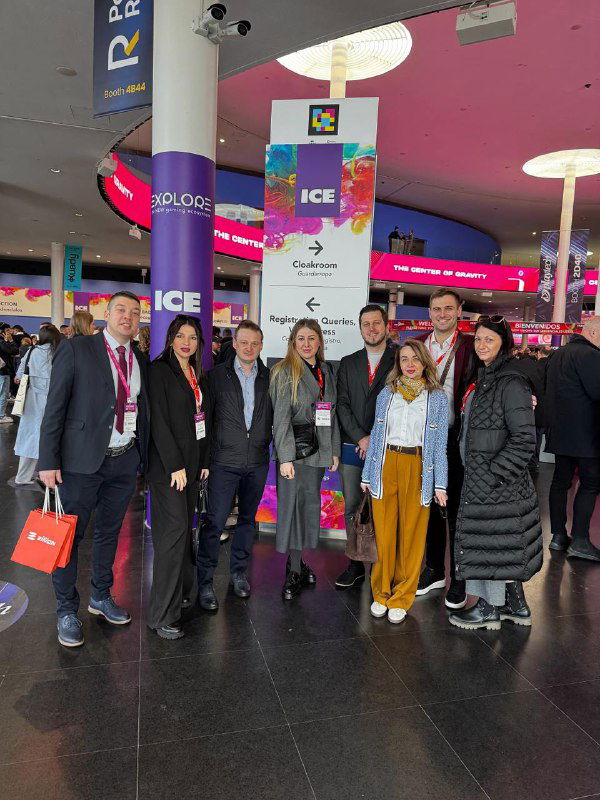 Group of Zillion Games team members and partners posing at the ICE Barcelona entrance beneath colorful event signage and large hanging banners.