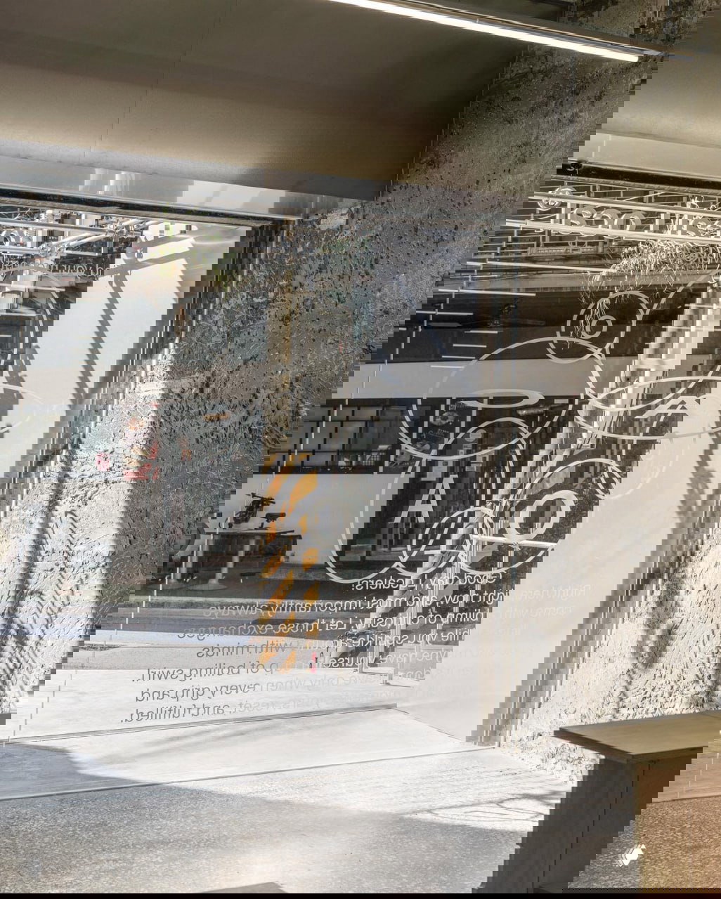 Вид изнутри на стеклянную дверь с нарисованными кругами и буквами, солнечные тени и урбанистическая сцена за витриной кофейни LocalLocal.