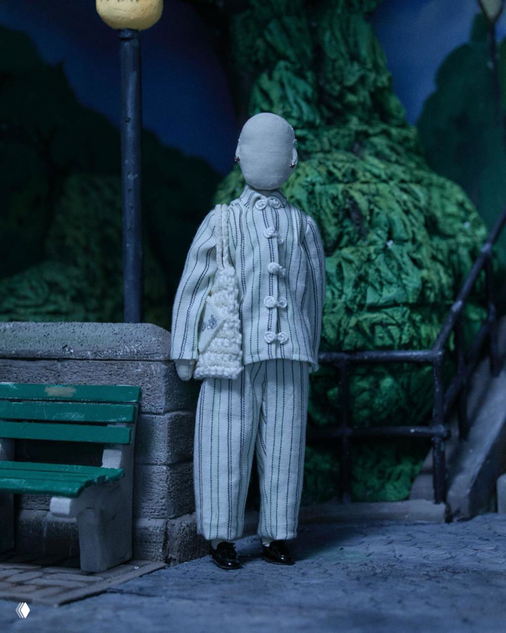 Миниатюрная фигура в полосатом светлом костюме стоит на тротуаре миниатюрной сцены — точная текстура тканей и аксессуаров.