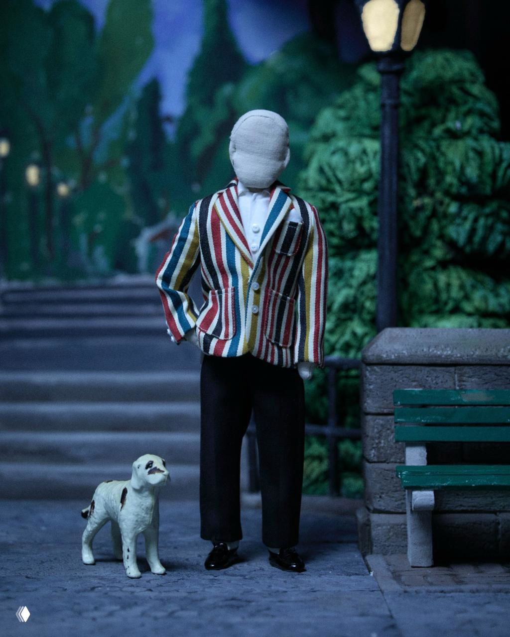 Кукла в полосатом пиджаке и чёрных брюках прогуливается по миниатюрному парку рядом с маленькой фигуркой собаки.