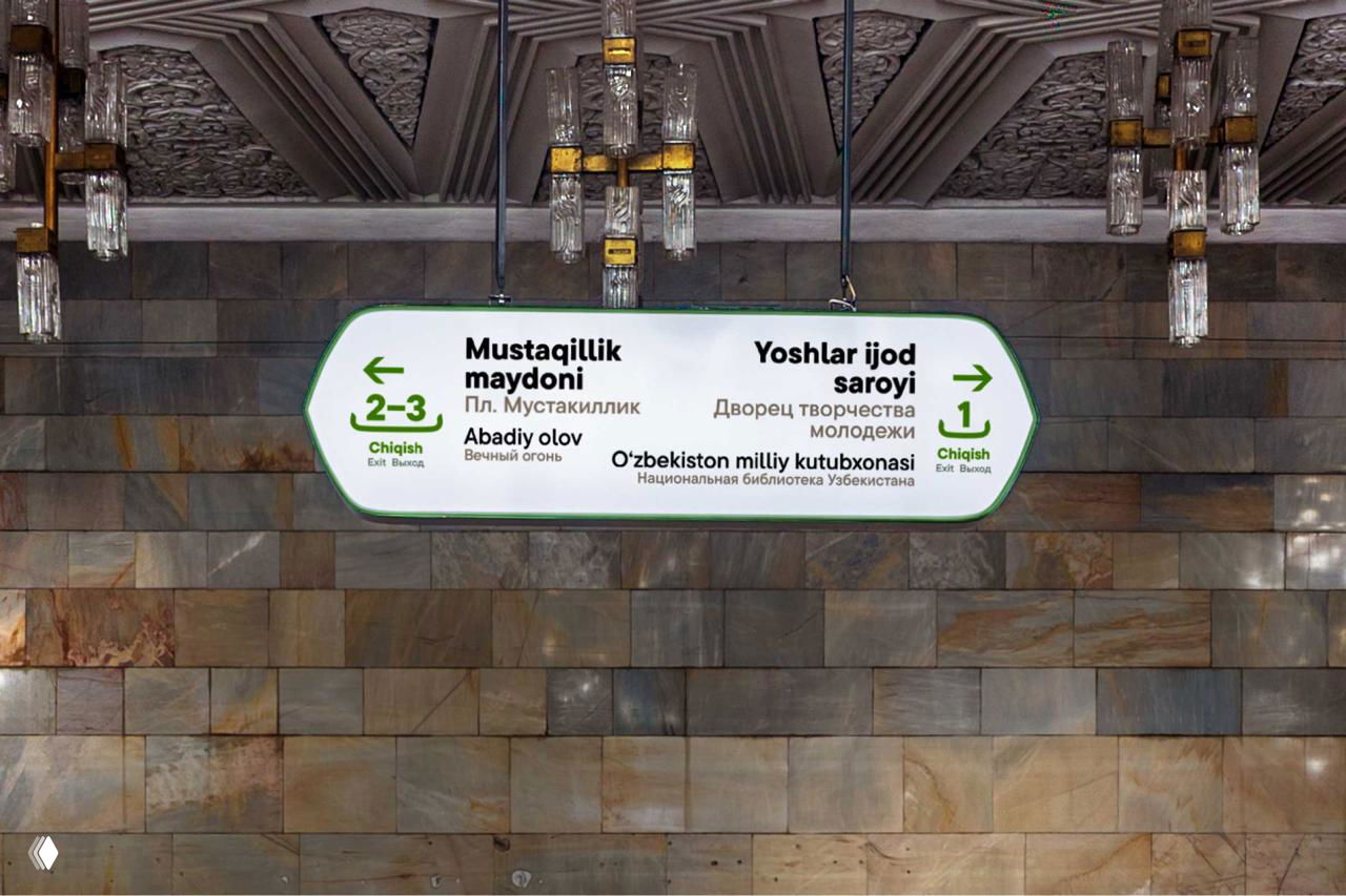 Вид вниз по эскалаторной лестнице: овальная настенная табличка с маршрутами и указанием станции Mustaqillik maydoni, люди спускаются по ступеням.