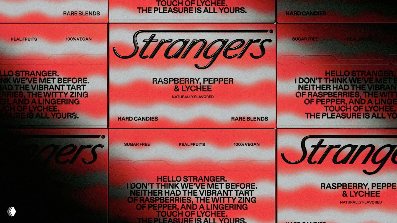 Крупный кадр лицевой стороны коробок Strangers: текстовые блоки, лозунг и контрастные размытые полосы в розово‑красной палитре.