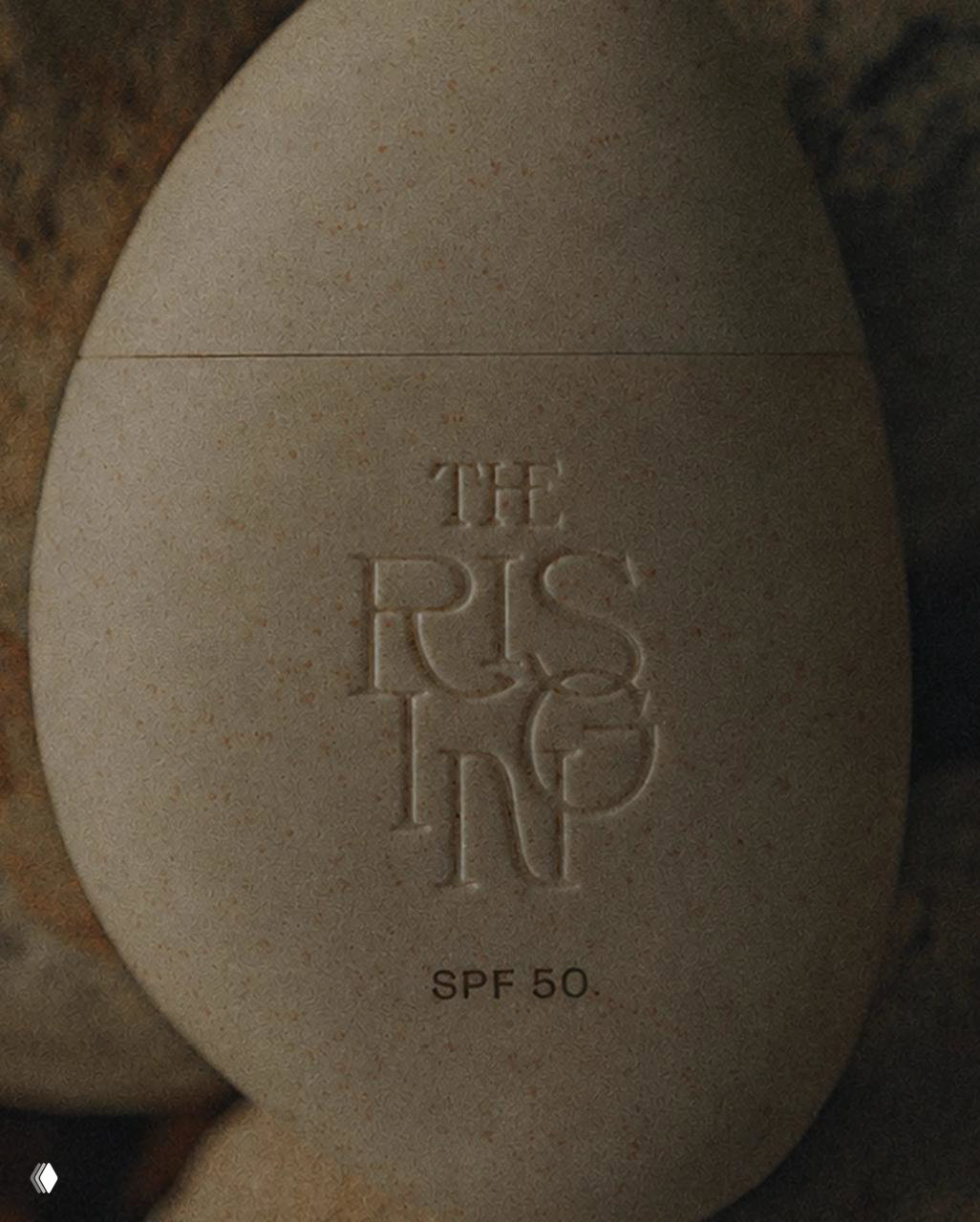 Крупный план тиснёного названия бренда The Rising на флаконе, видна зернистая текстура материала и маркировка SPF 50 у основания.