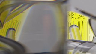 Кадр инсталляции с размытыми отражениями и желтыми постерами на заднем плане; ощущение движения и взаимодействия с камерой.