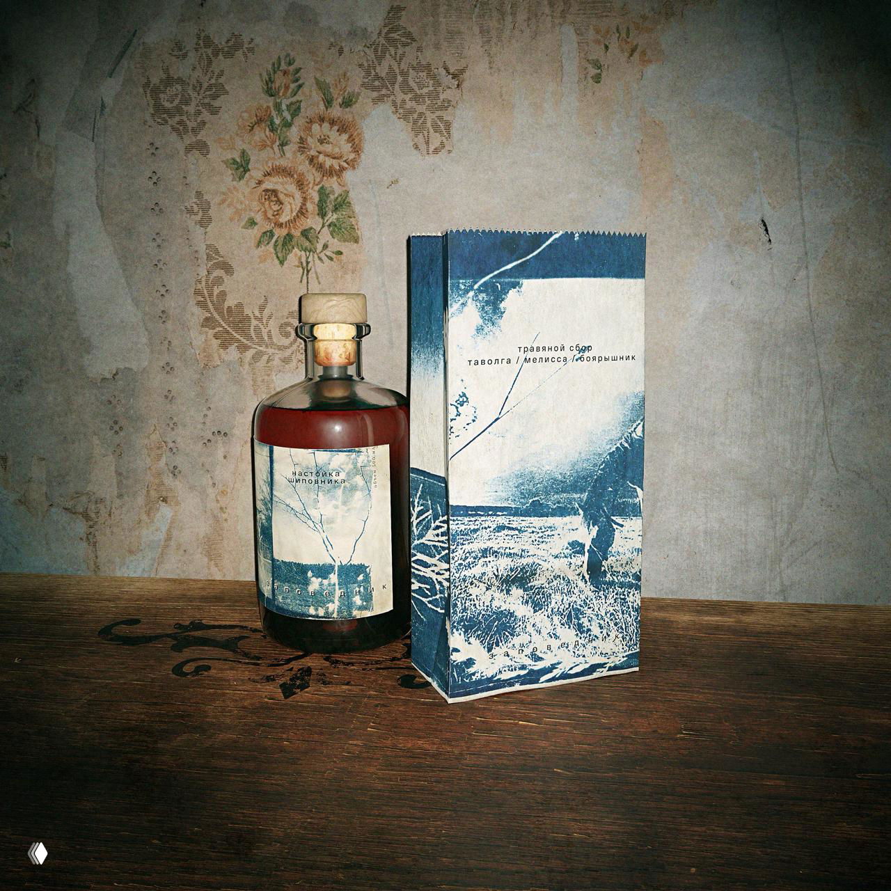 Бутылочка и коробка с сине-белыми иллюстрациями на фоне старой обоевой текстуры, подчёркивающие аутентичную атмосферу бренда.