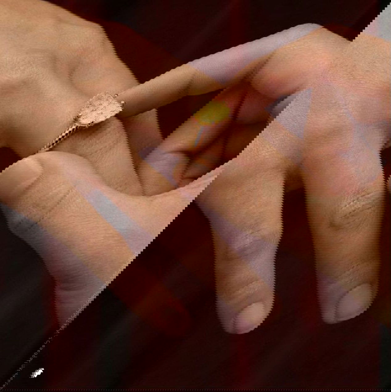 Руки надевают золотое кольцо с миниатюрным чипсом на палец; съемка крупным планом, акцент на текстуре кожи и металла.