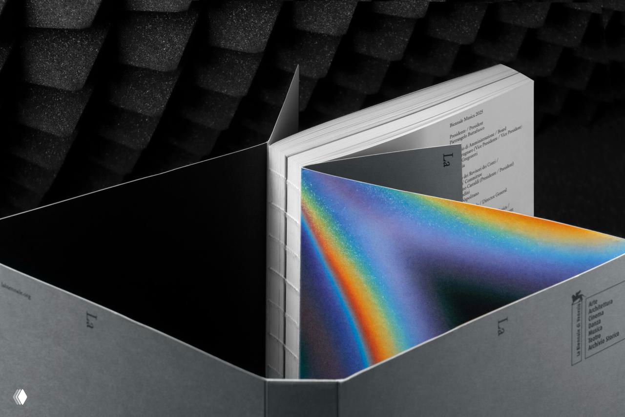 Ближний план раскрытого каталога с видимой тетрадной переплёткой и яркой радужной страницей, контраст на фоне акустической пены.