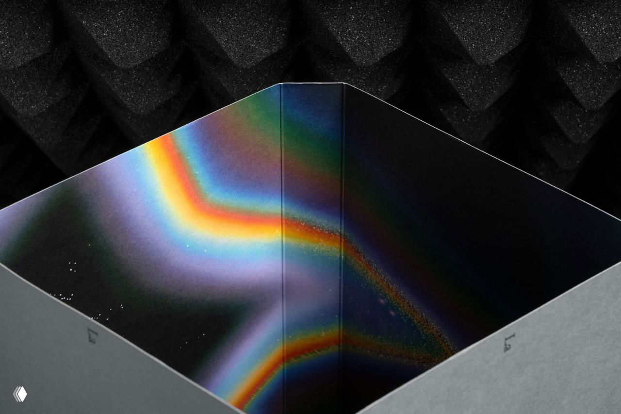 Вид сверху на внутреннюю часть коробки каталога: чёрная коробка и широкая радужная иллюстрация в форме звезды с градиентными переливами.