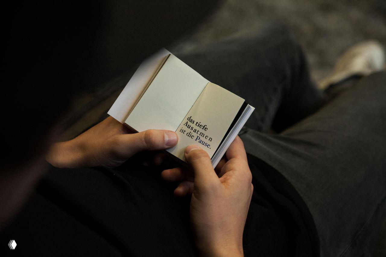 Крупный план рук, листающих небольшую книгу с разнообразными макетами; видно сочетание фотографий и типографических композиций.