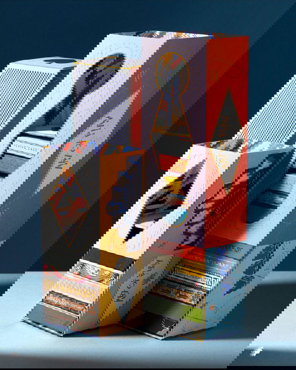 Два вертикальных бокса Art of Play на синем фоне: вырезы в упаковке, геометричные узоры и декоративное фольгирование на корешках и лицах коробок.