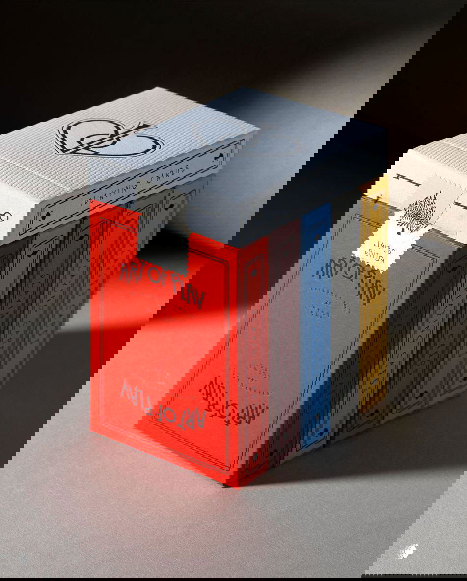 Красно-белая коробка Art of Play с рядом узких колод в разноцветных рубашках — крупный план показывает текстуру бумаги и аккуратное тиснение элементов логотипа.