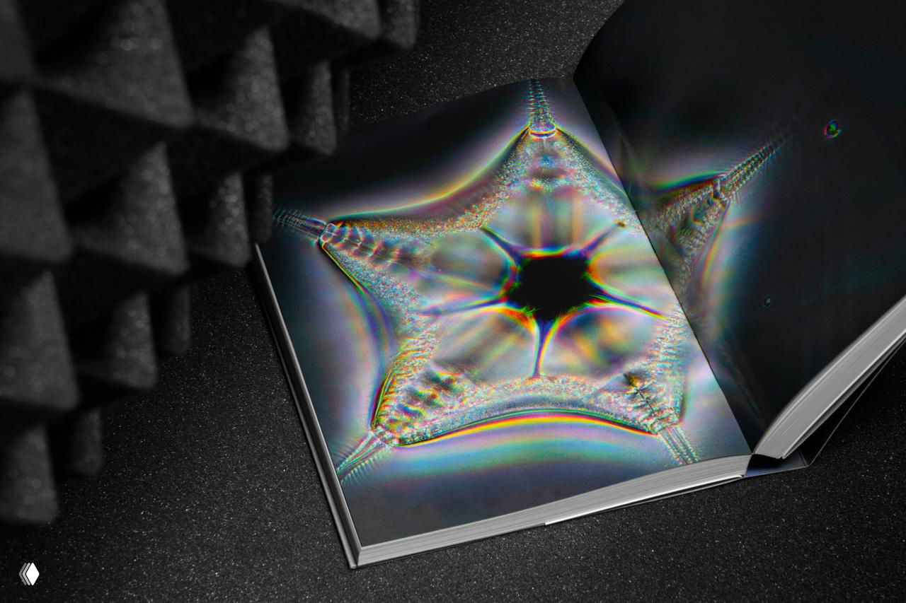 Разворот книги с крупной абстрактной радужной формой в виде размытой звезды, композиция подчёркнута мягким боковым освещением.
