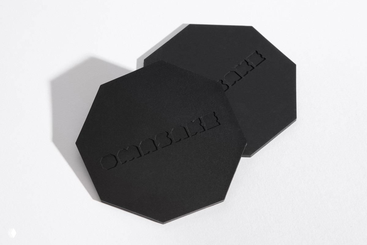 Черные восьмиугольные подставки для стаканов с вырезанным логотипом — предметы фирменного стиля, подчёркивающие геометрическую концепцию и тактильную отделку