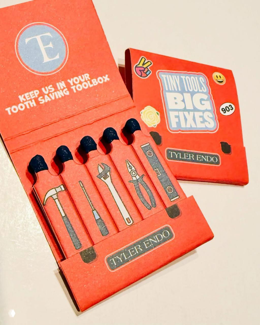 Красная коробка 'Tiny Tools' с пиктограммами инструментов: открытая упаковка и пять спичек с изображениями молотка, пассатижей и других инструментов.