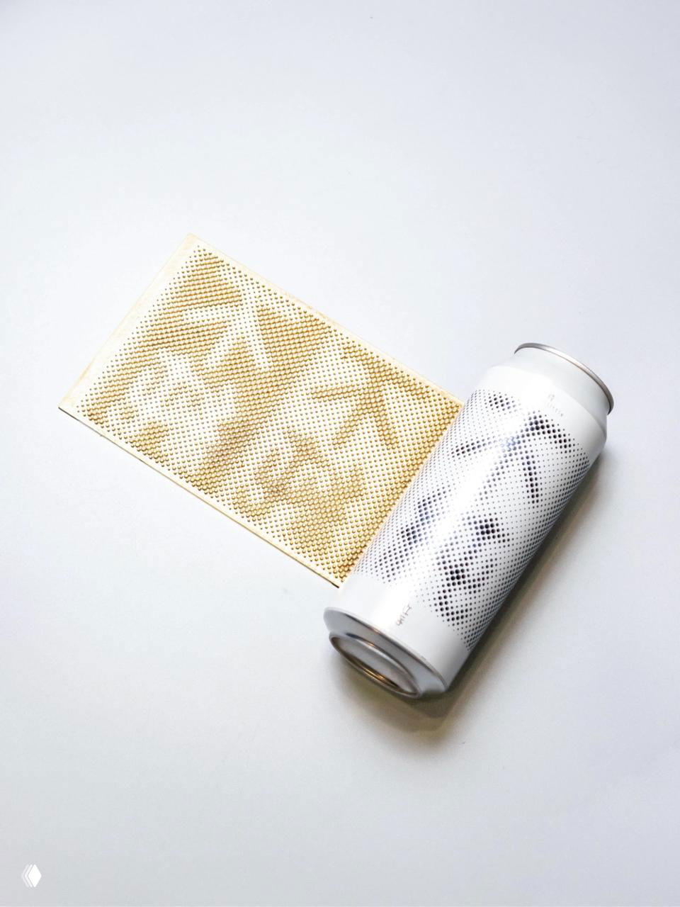 Банка рядом с оттиском растра на золотистой бумаге: видна связь между печатным оттиском и конечным видом упаковки на металле