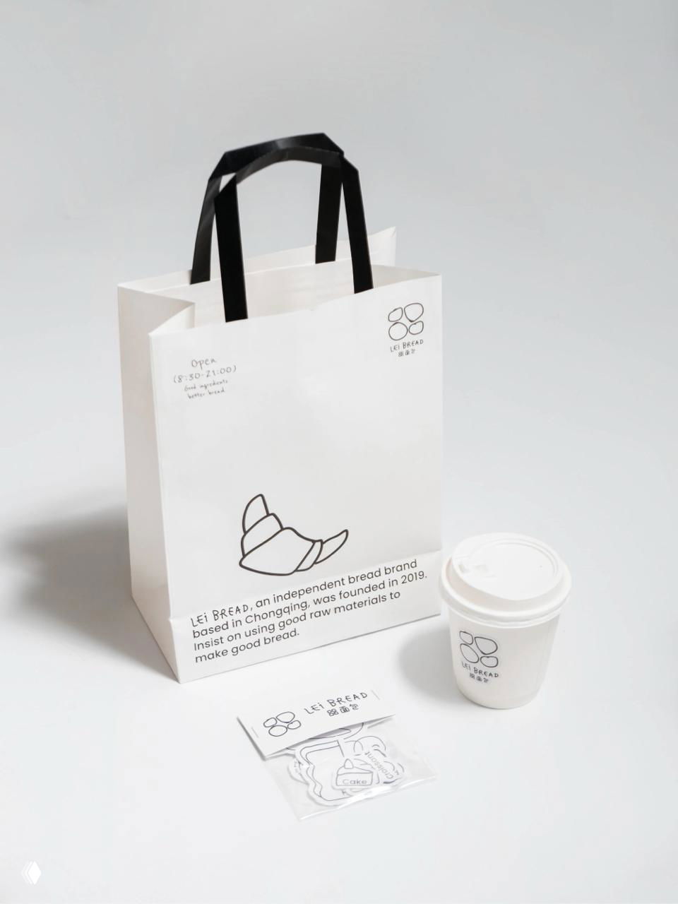 Студийное фото белого бумажного пакета Lei Bread с черными ручками и минималистичной маркировкой на нейтральном светлом фоне для показа упаковки.
