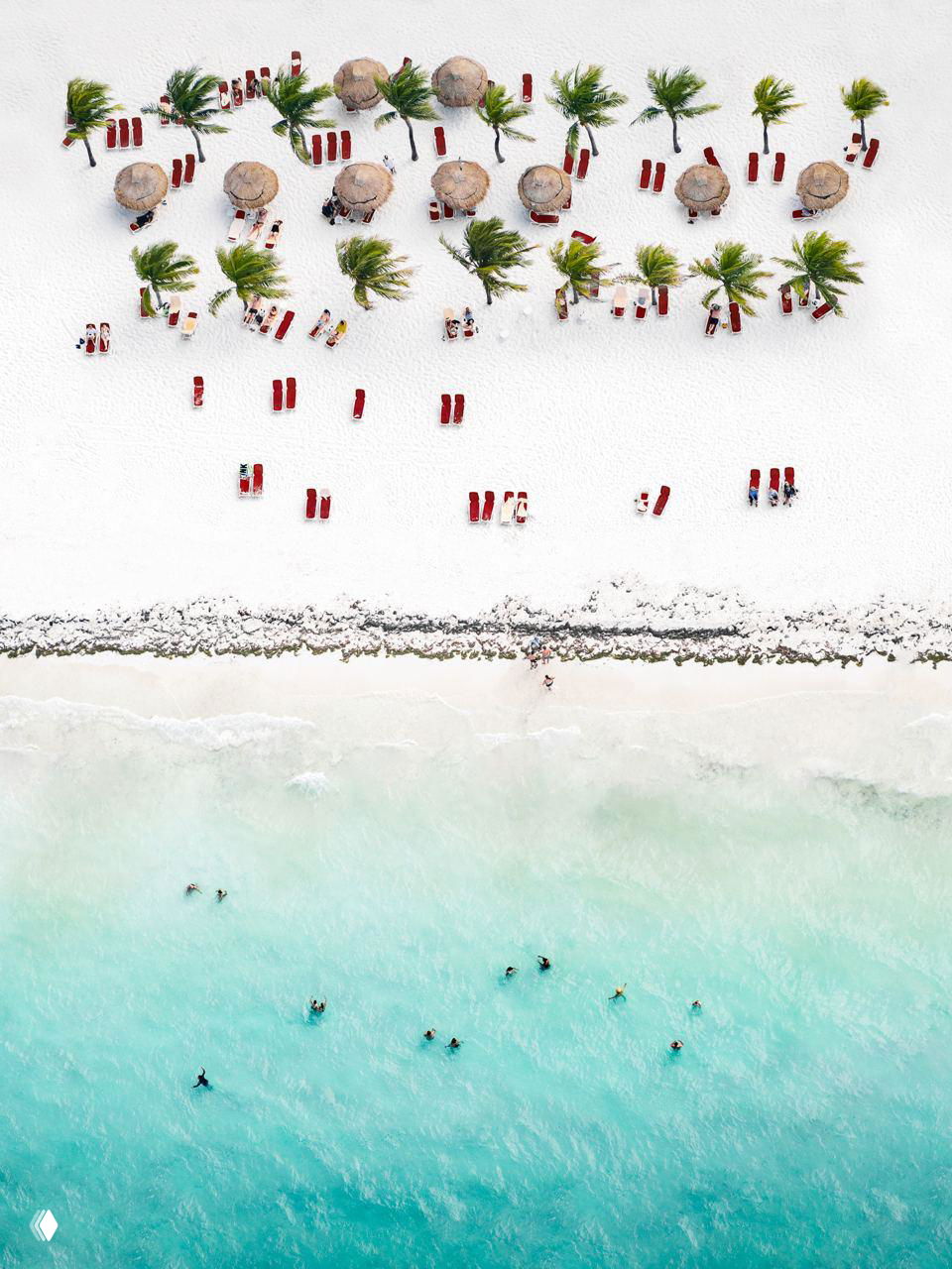 Вид сверху на линию шезлонгов и зонтов на белом карибском песке, люди в воде напоминают крошечные точки на фоне бирюзы.