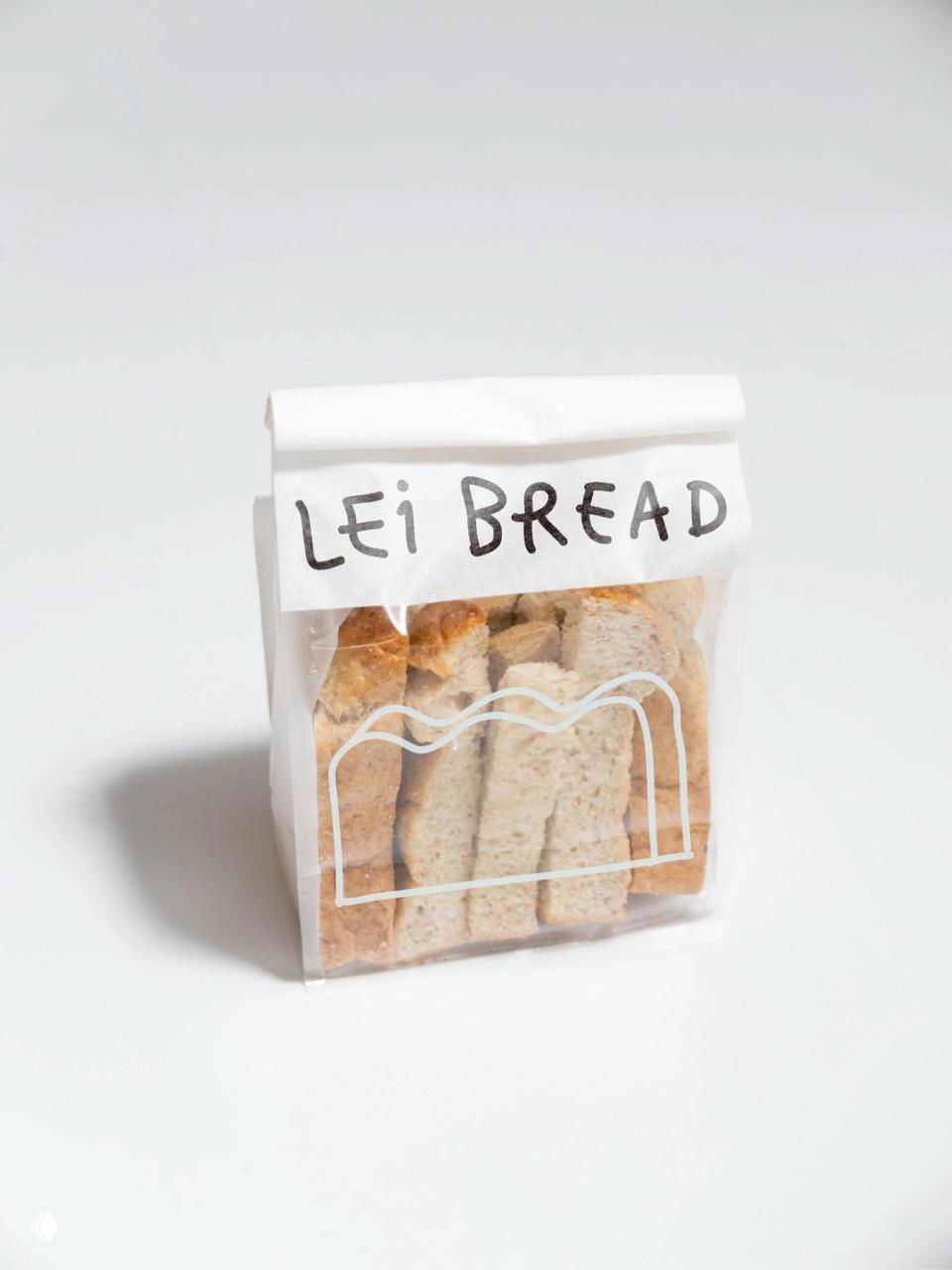 Пакет с нарезанным хлебом Lei Bread: белая бумажная упаковка с маркой и линейной иконкой хлеба на светлом нейтральном фоне студии.
