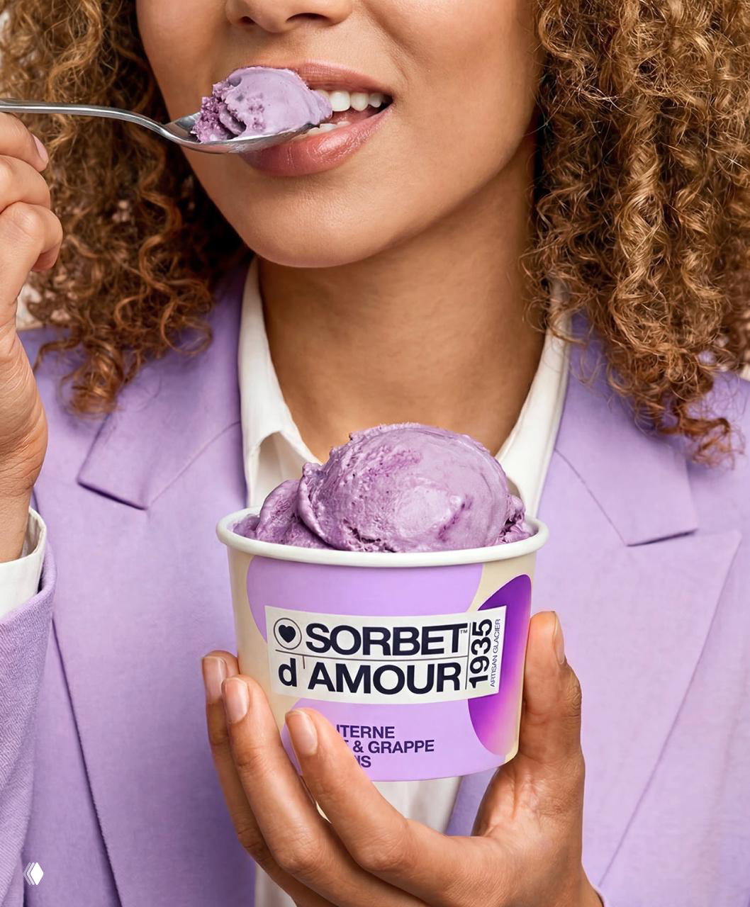 Женщина держит стаканчик Sorbet d'Amour с фиолетовым сорбетом и ест ложкой; упаковка в руках подчёркивает применение бренда в реальном использовании.