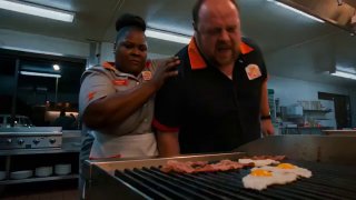 Сцена на кухне: две фигуры у гриля — крупная повариха и мужчина, жарящий еду; бытовой ресторанный интерьер и характерная комичная ситуация на переднем плане.