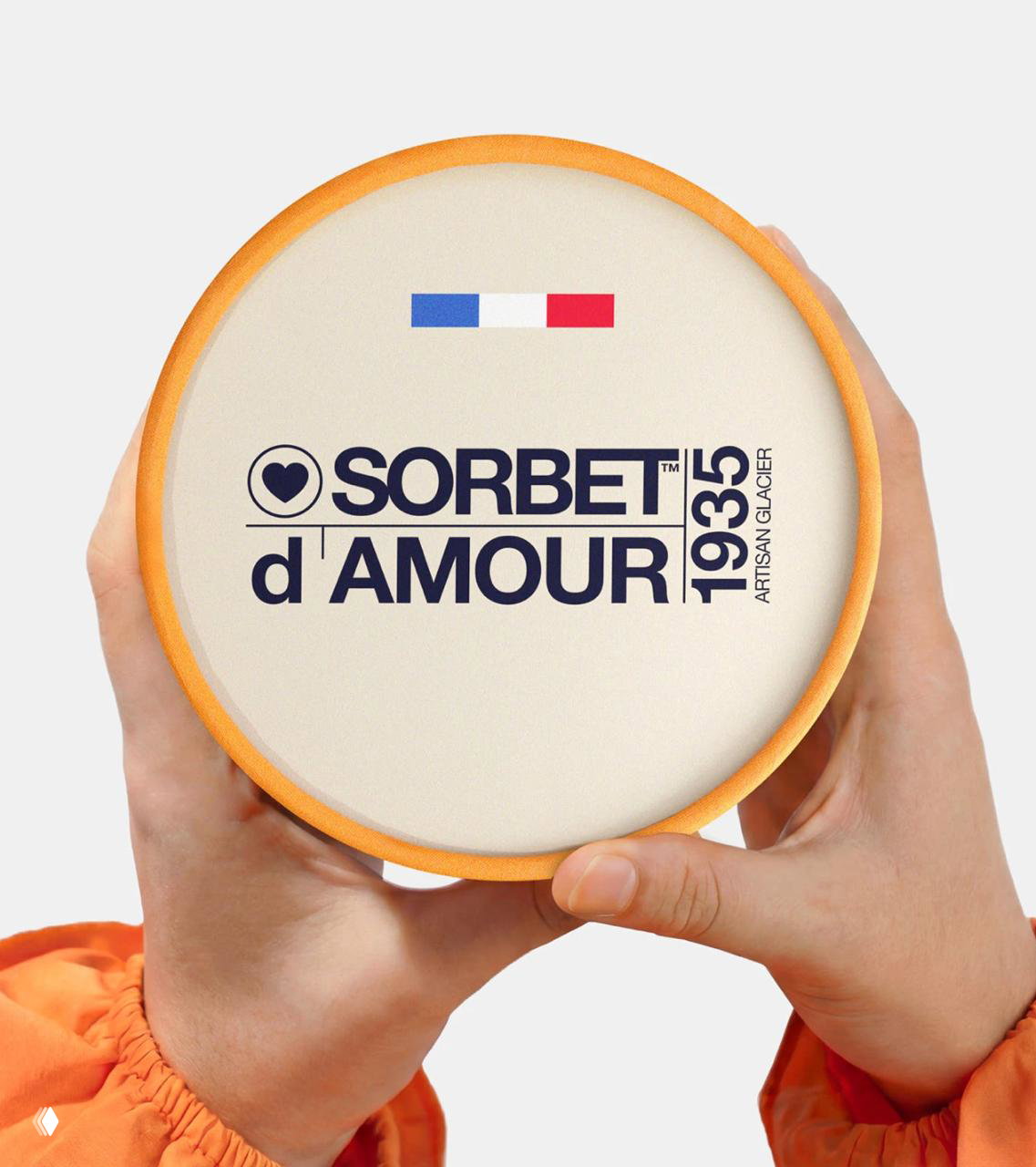Крупный план крышки в руках, минималистичный логотип Sorbet d'Amour и отметка 1935, светлый фон подчёркивает типографику и форму упаковки.