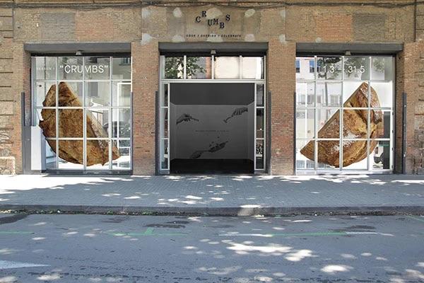 Фасад с витриной, оформленной крупными графическими элементами хлеба и окнами, показывающий наружную адаптацию айдентики Crumbs для входа в пространство.