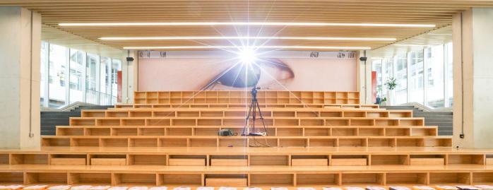 Внутренний зал лекций форума с рядом деревянных сидений и установленной проекторной техникой — контекст площадки мероприятия.