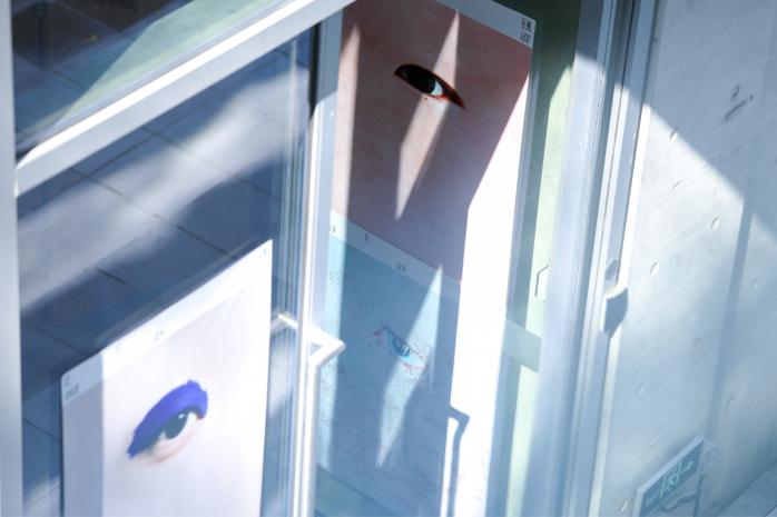 Солнечные блики и отражения на стеклянной двери, через которую видны постеры с изображениями одного глаза — игра света и графики.