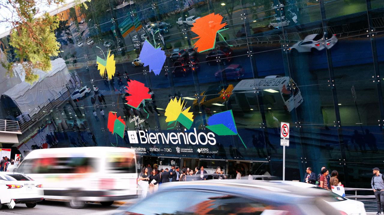 Фасад выставочного центра с крупными декоративными элементами‑цветами айдентики, люди и автомобили на переднем плане, городской контекст применения бренда.