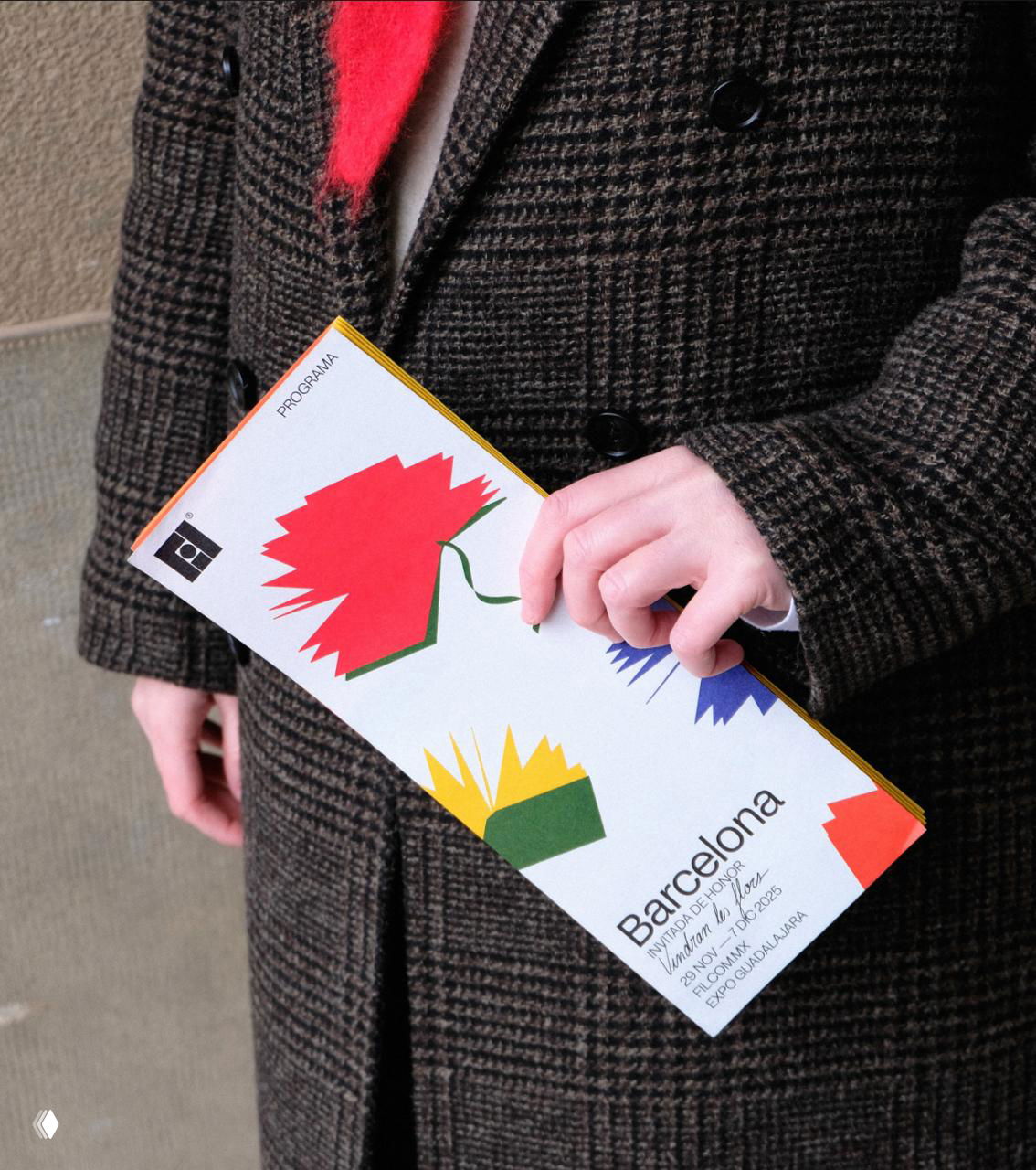 Человек держит печатную программу ярмарки с иллюстрациями цветка‑книги; кадр демонстрирует носитель коммуникации в руке посетителя.