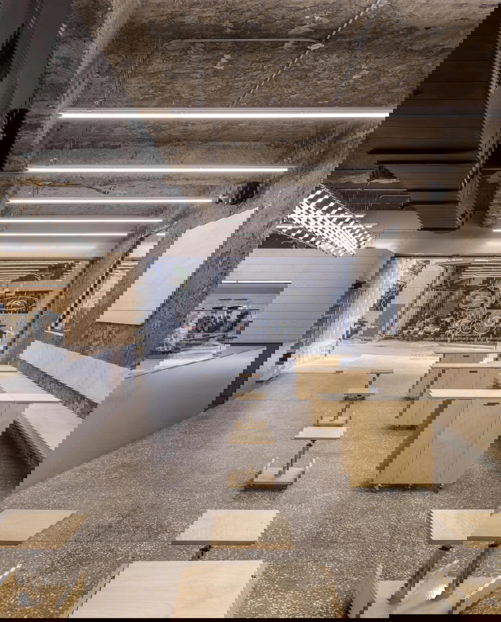 Общий вид зала кофейни: ряд минималистичных столиков и лавок из светлой фанеры, открытый проход к витрине с графикой кругов и букв.