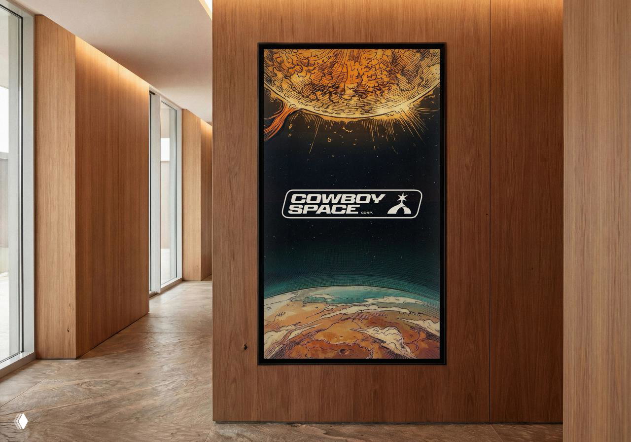 Постер Cowboy Space в деревянной раме в интерьере: логотип на фоне художественной космической иллюстрации с планетой и солнцем, презентация бренда в пространстве.