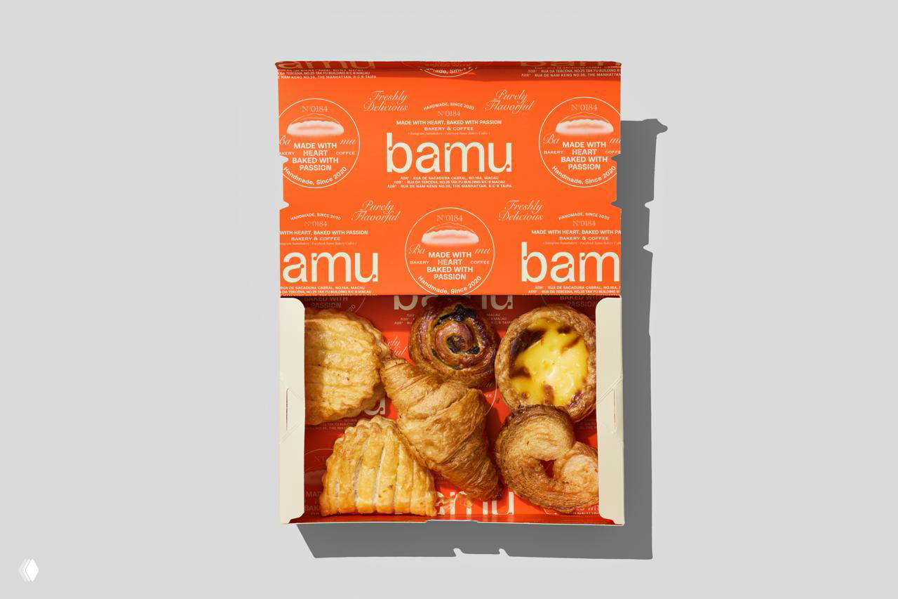 Открытая коробка Bamu с набором выпечки: видны круассаны, пирожные и бумажная вставка с повторяющимся брендингом в оранжевой гамме.