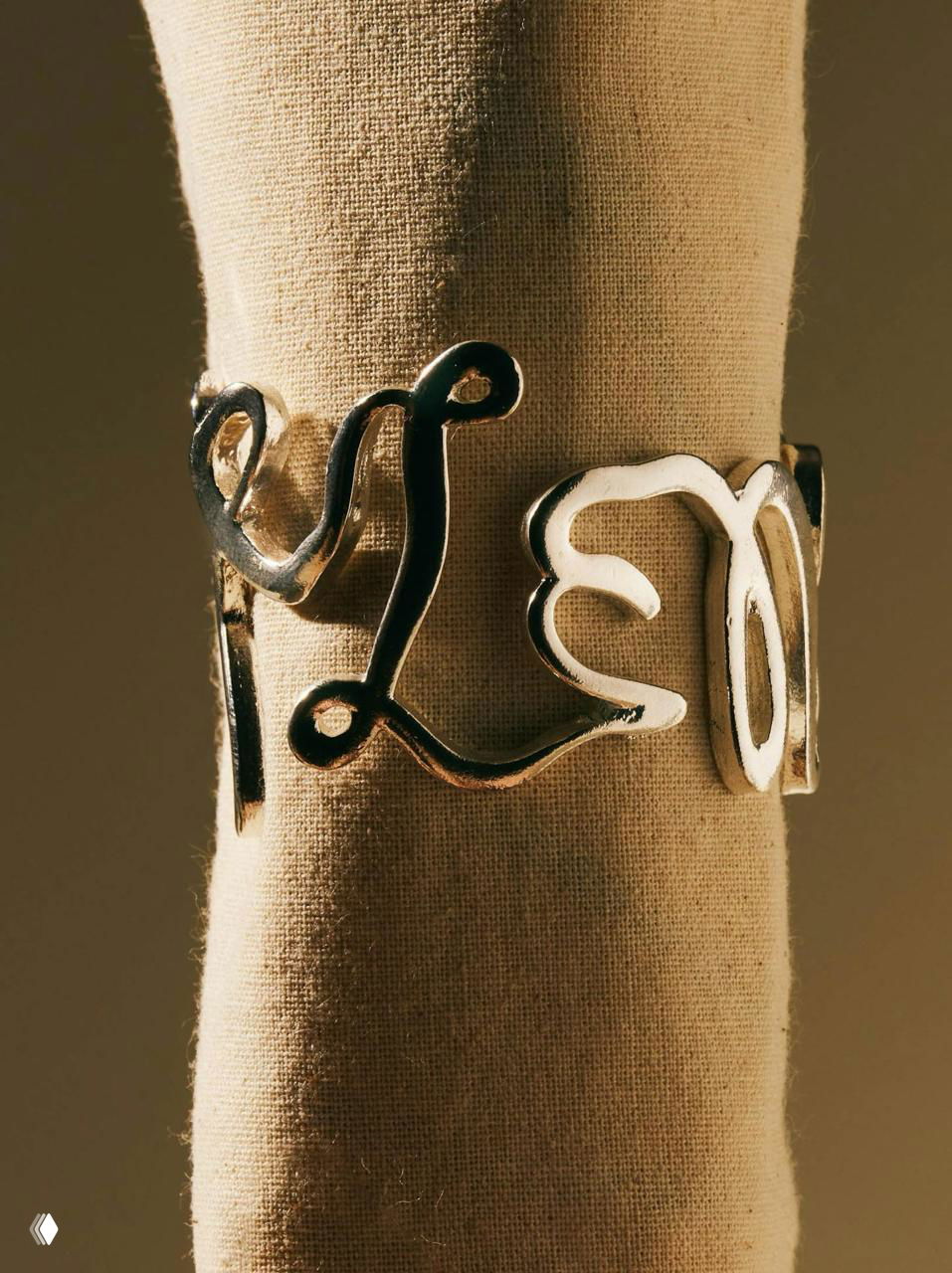 Металлическое кольцо‑салфетник в форме завитка с буквами Selene на манекене; крупный план, блестящая поверхность и художественный брендинг.