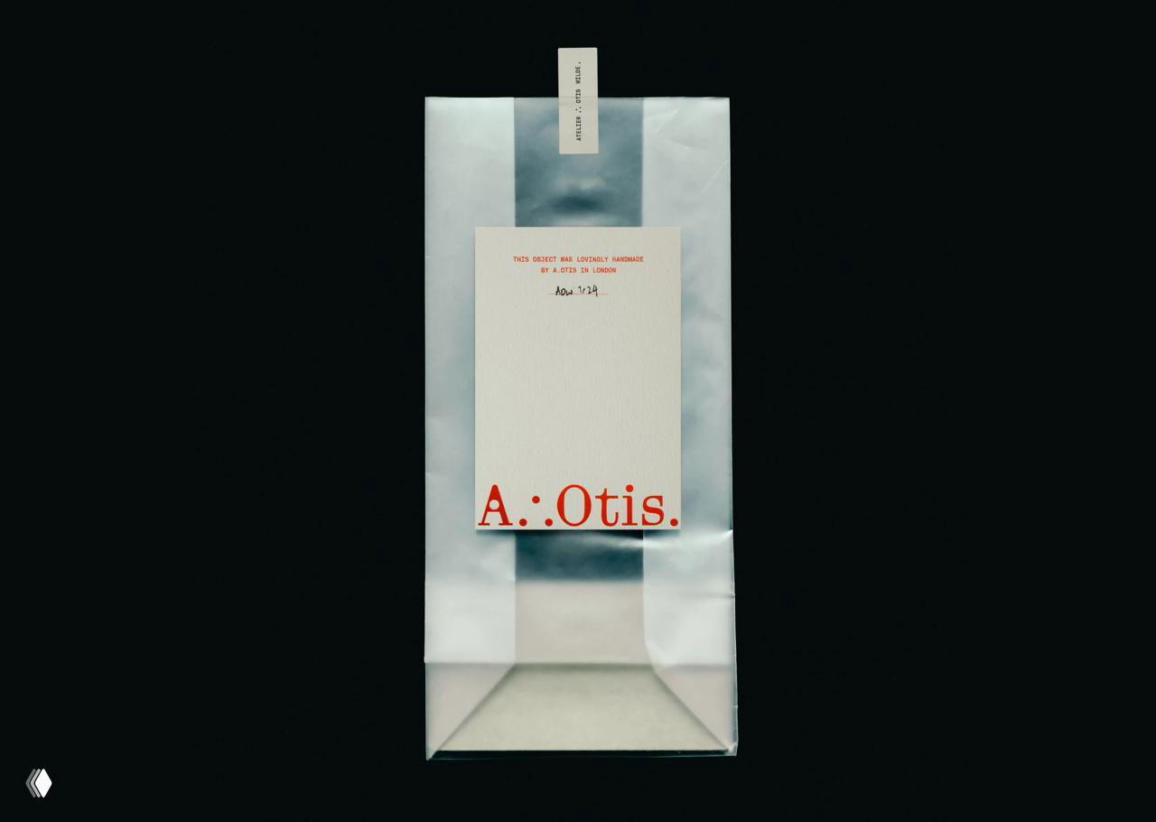 Изображение упаковки и бумажной бирки бренда A.Otis на тёмном фоне: белый пакет, типографика и минималистичная подача фирменного знака.
