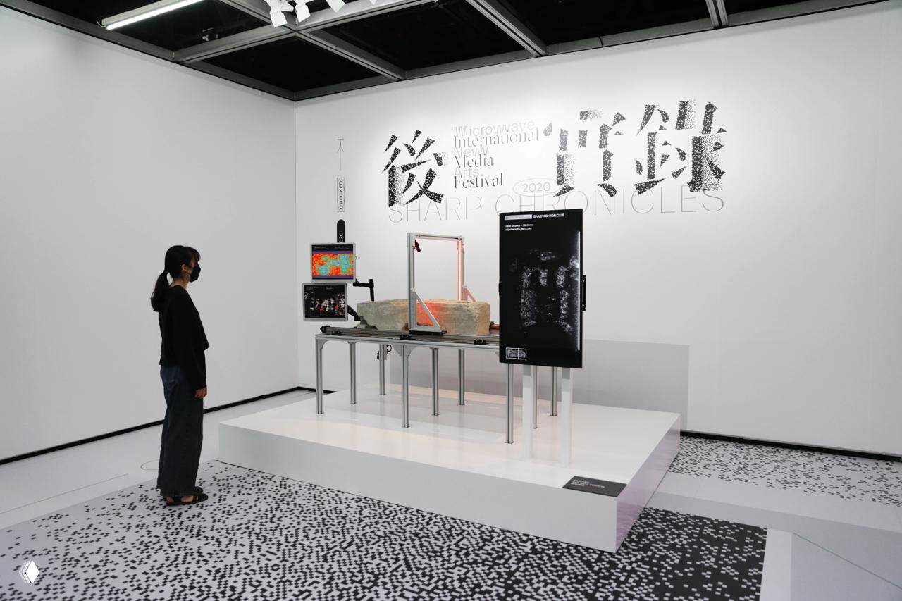Белая выставочная зона с инсталляцией и панелями, логотип Sharp Chronicles на стене; посетитель наблюдает навигацию и экспонаты