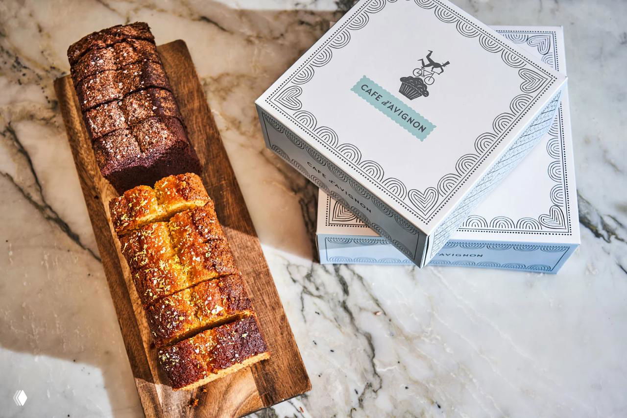 Коробки и хлеб на деревянной доске: макеты упаковки с декоративным узором и традиционной типографикой для кондитерской.