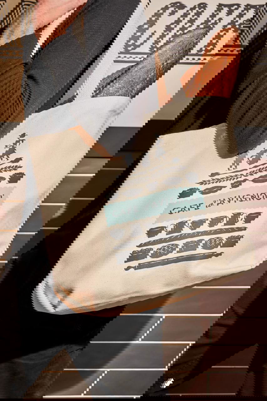 Холщёвая сумка с логотипом CAFE d’AVIGNON и багетом внутри — пример мерча и нанесения графики на текстиль.