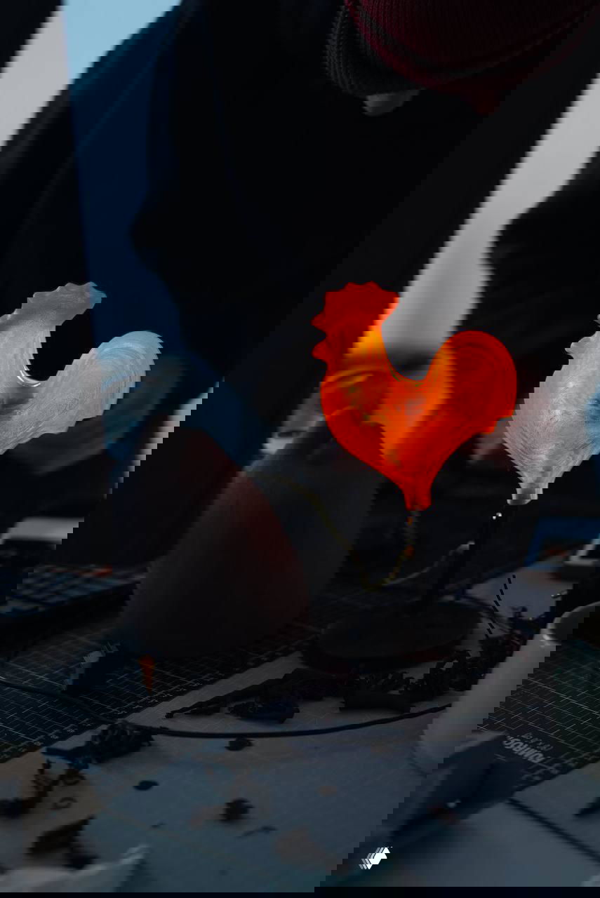 Яркая оранжевая лампа в форме петуха на подставке, тёплый свет и фокус на силуэте, мастерская дизайнера на фоне