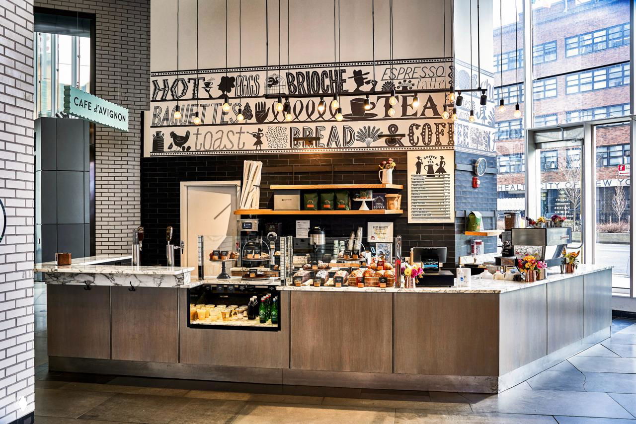 Широкий план прилавка кафе с витриной, витринами с выпечкой и большой настенной росписью — демонстрация айдентики в пространстве заведения.