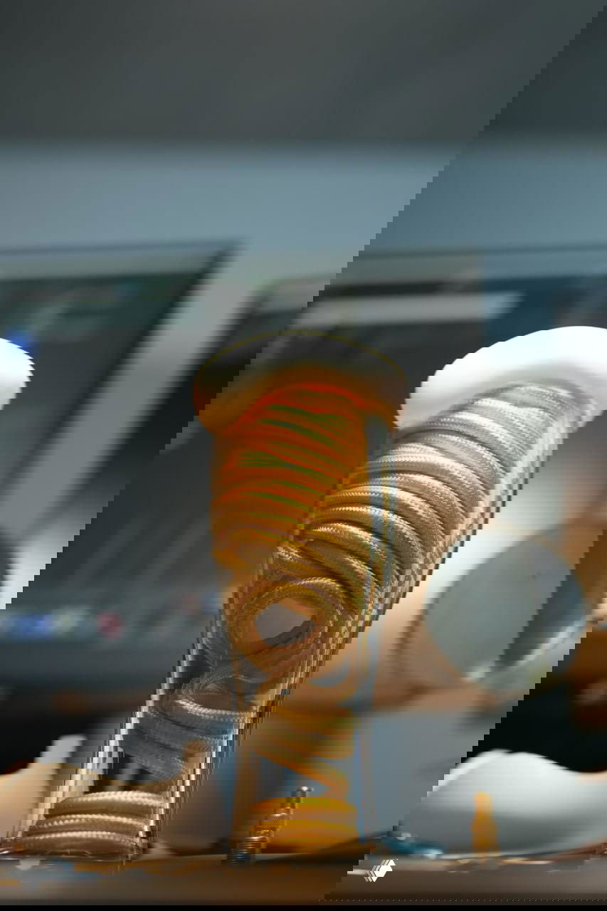 Прозрачная ёмкость с намотанным внутри жёлтым кабелем и мягким светом сверху, рабочая поверхность и монитор позади