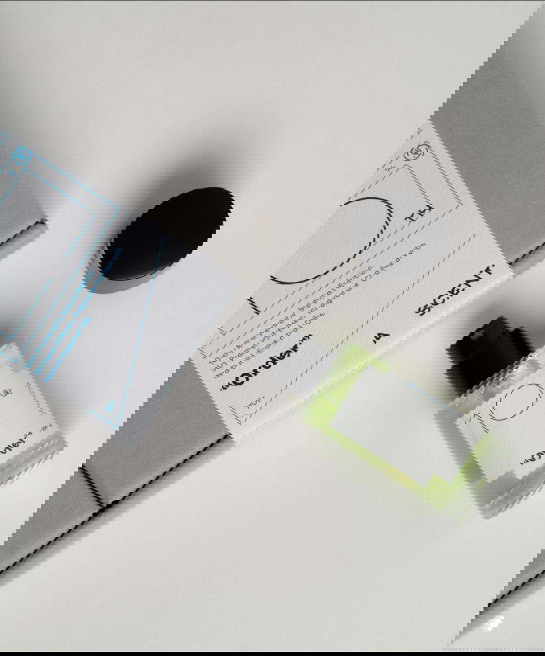 Мини‑флакон аромата с прозрачным зелёным содержимым рядом с серой коробкой и инструкцией — композиция подчёркивает минимализм и технические чертежи на бумажной этикетке.