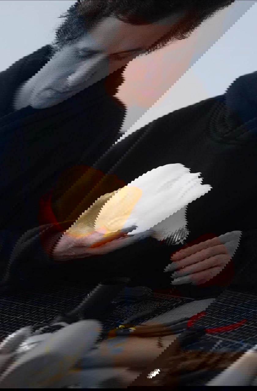 Дизайнер держит светящуюся лампу в форме человеческого лица, процесс сборки и внимание к деталям в мастерской