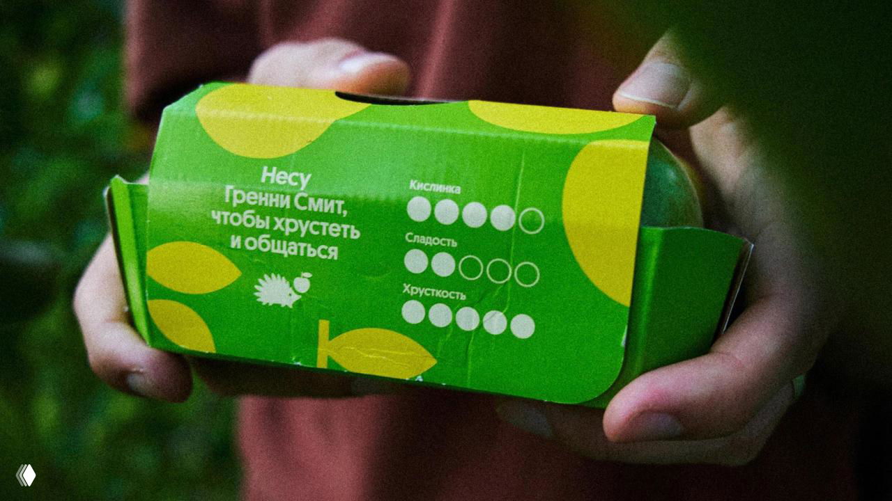 Крупный план зелёной упаковки сорта Granny Smith: видна графическая шкала 'кислинка/сладость/хрусткость' и короткие описания сорта.