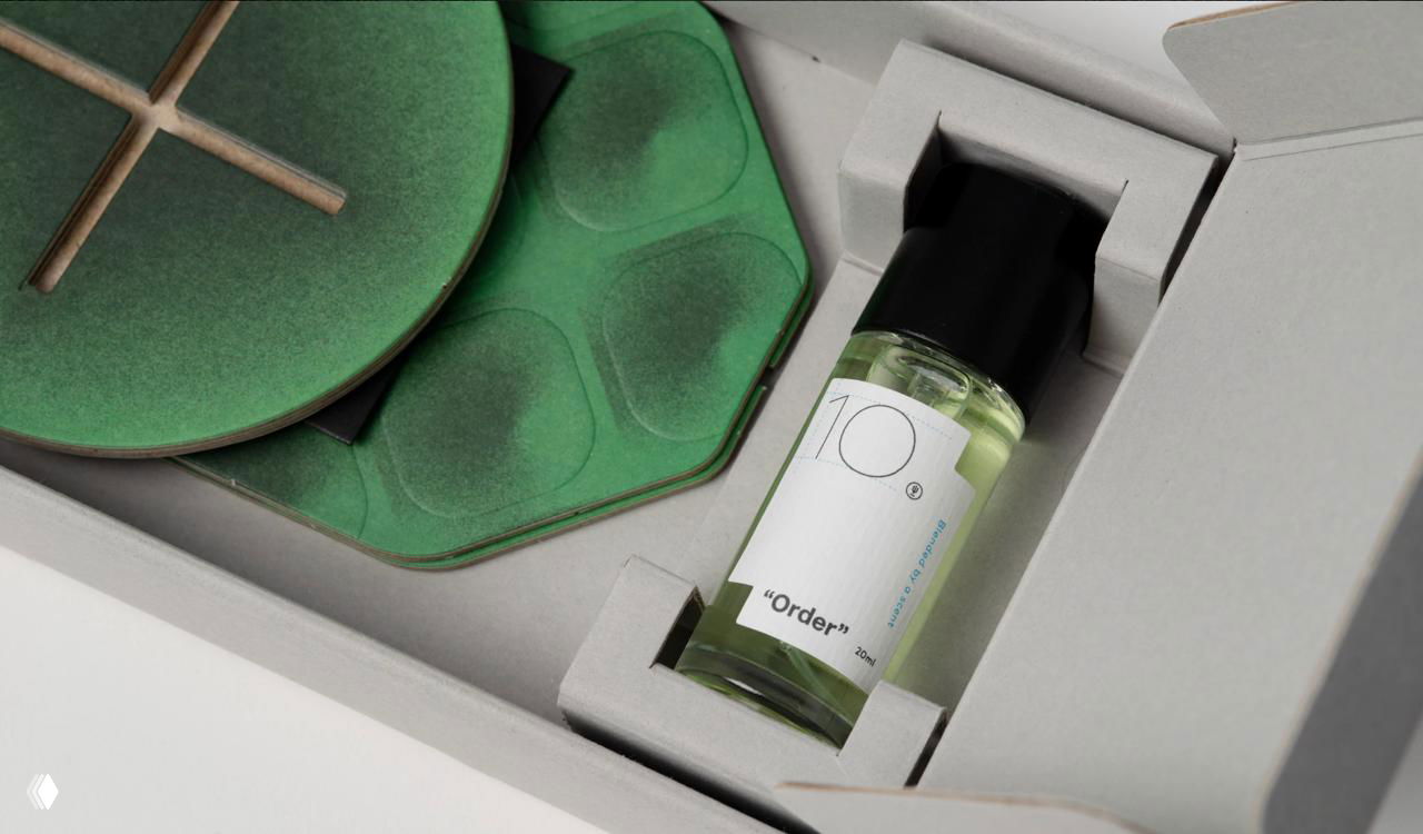 Внутренний вид коробки: флакон аромата закреплён в картонной вставке, рядом лежат модульные детали зелёного картона для сборки объёмного диффузора.