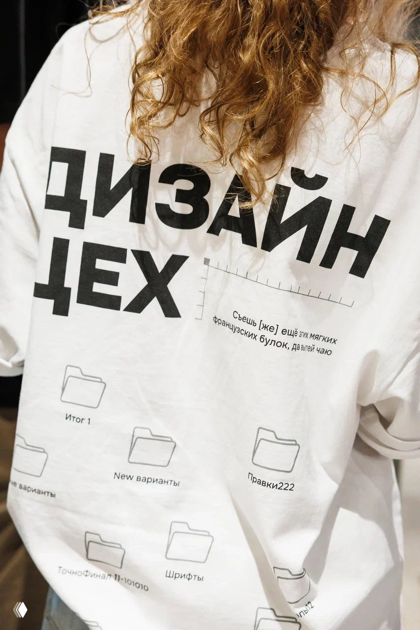 Крупный план белой футболки с крупной печатью «ДИЗАЙН ЦЕХ» и графикой папок и надписей — пример мерч-концепта с интенсива.